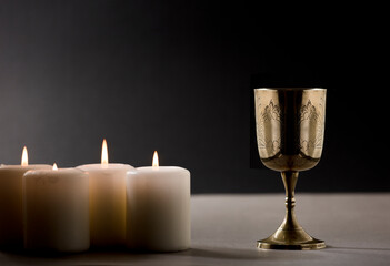 golden christian chalice with burning candles on gray altar black background night