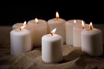 Fototapeta na wymiar bullying concept, composed by group of lit candles, on sand with black night background