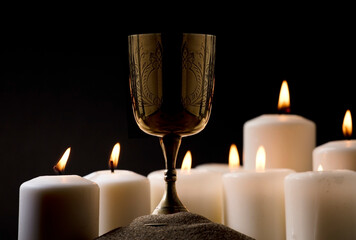 golden christian chalice on ground with burning candles black background night