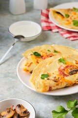 Hearty wheat pancakes with ham, mushrooms and cheddar cheese on a white plate on a gray concrete background. International Pancake Day, Maslenitsa.