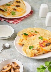Hearty wheat pancakes with ham, mushrooms and cheddar cheese on a white plate on a gray concrete background. International Pancake Day, Maslenitsa.