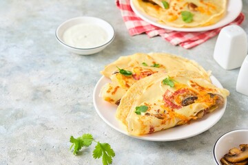 Hearty wheat pancakes with ham, mushrooms and cheddar cheese on a white plate on a gray concrete background. International Pancake Day, Maslenitsa.