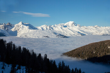 Montagnes enneigée et forêt entourées de nuages pendant l'hiver avec un ciel bleu. 