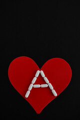 Corazón rojo y píldoras blancas sobre fondo negro, espacio para texto en la parte superior.
