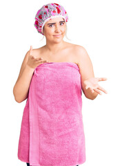 Young caucasian woman wearing shower cap and towel clueless and confused expression with arms and...