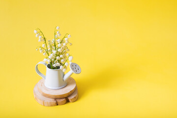 Lilies of the valley bouquet in a decorative watering can on a yellow background with copy space