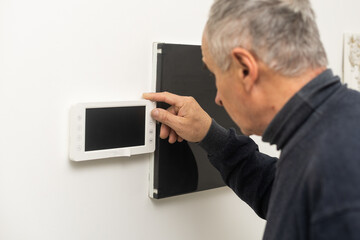 an elderly man repairs an intercom. © Angelov