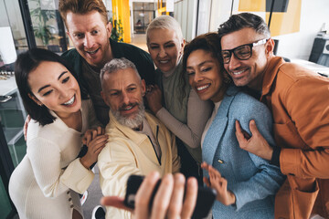 Happy multiethnic colleagues taking picture on smartphone in office