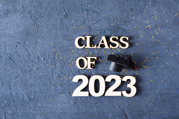 Class of 2023 concept. Wooden number 2023 with graduated cap on dark concrete background with tinsel