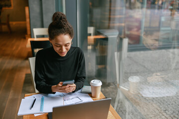 Woman architect use phone during working in cafe sitting near window. Distance work concept