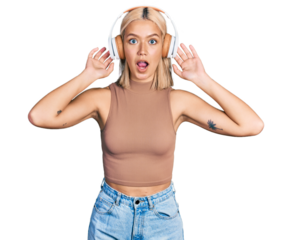 Beautiful young blonde woman listening to music using headphones afraid and shocked with surprise and amazed expression, fear and excited face.