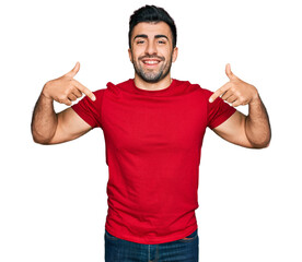 Hispanic man with beard wearing casual red t shirt looking confident with smile on face, pointing oneself with fingers proud and happy.