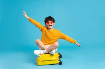 Asian boy pulling suitcase on blue background