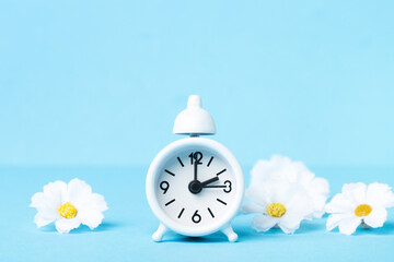 White Alarm Clock and Spring Daisy Flowers on Blue Background