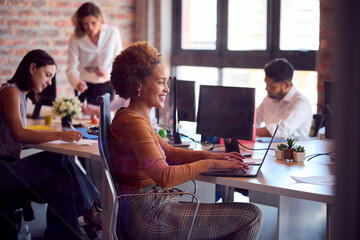Businesswoman Working On Laptop At Desk In Busy Multi-Cultural Office