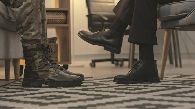 Low section of unrecognizable psychiatrist and veteran soldier sitting in front of each other at individual therapy session