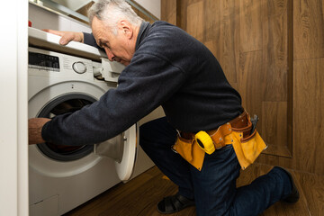 an elderly man repairs a washing machine