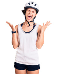 Beautiful young woman with short hair wearing bike helmet celebrating mad and crazy for success with arms raised and closed eyes screaming excited. winner concept