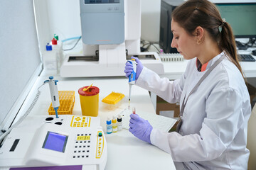 Female laboratory assistant uses special pipette to work with biomaterial - obrazy, fototapety, plakaty
