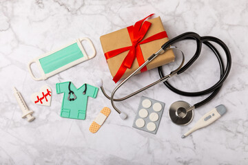 National Day of Doctors. Modern stethoscope, gift box and gingerbread in the form of medical supplies on a marble background. .Gingerbread in the form of a thermometer, a medical mask, a pill, a patch