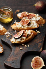 Delicious bruschetta with figs, cream cheese, pine nuts and honey on dark wooden board. Close up view, selective focus
