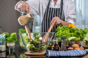woman chef mix fresh baby cos salad and pour salad dressing in glass blow. Organic Vegetables mix all green salad In glass bowl. Breakfast fresh salad and clean vegetable.