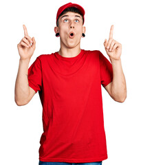 Young caucasian boy with ears dilation wearing delivery uniform and cap amazed and surprised looking up and pointing with fingers and raised arms.