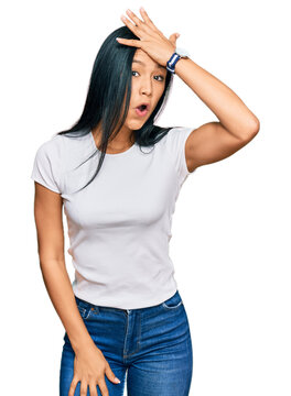 Beautiful hispanic woman wearing casual white tshirt surprised with hand on head for mistake, remember error. forgot, bad memory concept.