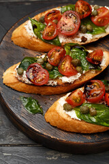 Traditional italian bruschetta with cherry tomatoes, cream cheese, basil leaves, capers and balsamic vinegar on wooden cutting board. Side view, close up