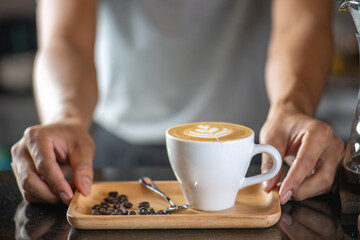 White ceramic cups of cappuccino with latte art Barista make coffee by pouring spills hot milk cream on black coffee. Barista serve holding cup of hot latte and coffee beans on wooden table cafe shop