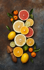 Set of various fresh citrus fruits with leaves and wooden juicer on dark concrete background. Healthy food backround. Flat composition. Top view