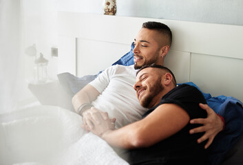 Male couple enjoying together and smiling while relaxing in bed at home.