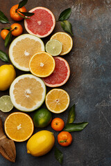 Set of various fresh citrus fruits with leaves and wooden juicer on dark concrete background. Healthy food backround. Flat composition with copy space. Top view