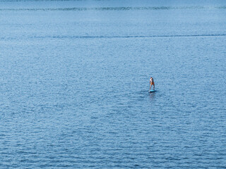 Naklejka premium Active recreation on the board on the big river. Tourism on sap boards. Outdoor water sports. Surfers, standing on a board, ride the waves. SUP surfing training. View of the city embankment