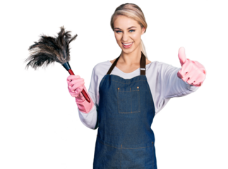 Beautiful young blonde woman wearing apron holding cleaning duster approving doing positive gesture with hand, thumbs up smiling and happy for success. winner gesture.