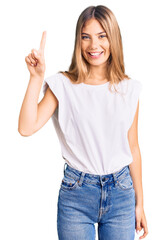 Fototapeta na wymiar Beautiful caucasian woman with blonde hair wearing casual white tshirt showing and pointing up with finger number one while smiling confident and happy.