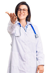 Young beautiful woman wearing doctor stethoscope and glasses smiling friendly offering handshake as greeting and welcoming. successful business.