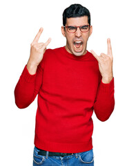 Handsome hispanic man wearing casual clothes and glasses shouting with crazy expression doing rock symbol with hands up. music star. heavy concept.