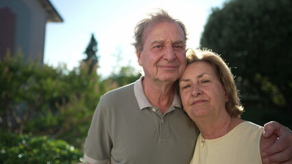 Fototapeta premium Portrait of a married senior couple standing outside. Older husband with arm around wife. Two elder people close up faces together. Love concept