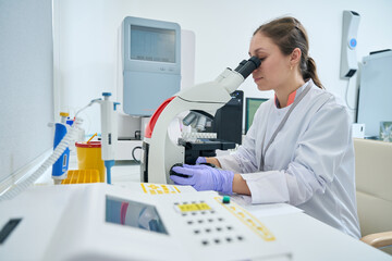 Laboratory employee looks into the eyepiece of microscope