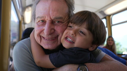 Obraz premium Grandson hugging grandfather while traveling by train on vacation. Child embraces senior grandparent cheek to cheek on railroad. Generational love