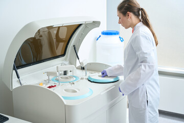 Woman in overalls stands in front of modern biochemical analyzer