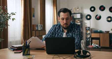 Concentrated beard young midlle aged man person with disabilities sitting at the table desk working online from home distance. Freelander concept in front of screen. Supportive operator executive job.