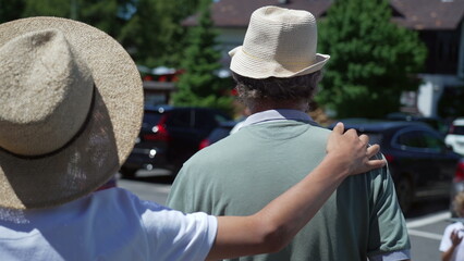 Back of grandfather and grandson wearing Panama Hats walking together. Teenager kid with arm around senior grandparent. Happy Family bonding concept