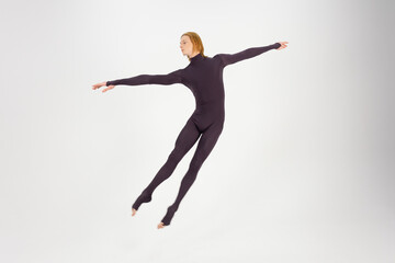 Fototapeta na wymiar Young athletic professional ballet dancer in a black unitard is in perfect shape, performing and jumping over a white background.