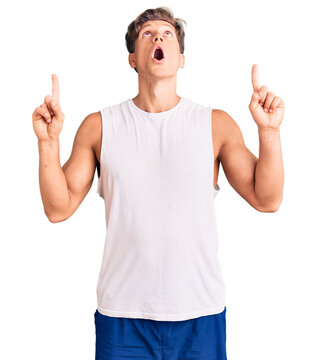 Young handsome man wearing sleveeless t shirt amazed and surprised looking up and pointing with fingers and raised arms.
