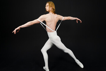 Fototapeta na wymiar Young athletic professional ballet dancer with a bare torso and white dance tights is in perfect shape, performing and posing over a black background.