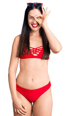 Fototapeta premium Young beautiful caucasian woman wearing bikini doing ok gesture with hand smiling, eye looking through fingers with happy face.
