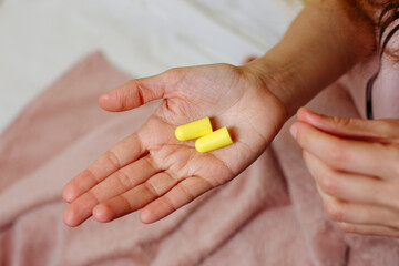 Close up of female hands and yellow earplugs. Woman holding a earplugs. Pink background. Copy space