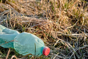 Crumpled plastic bottle covered with ice and snow in frozen dry grass. Green with red bottle cap....